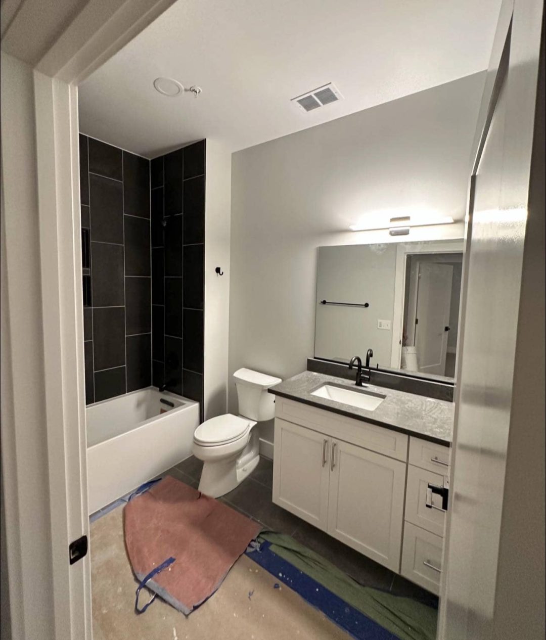 Modern bathroom featuring a black-tiled shower, white vanity with a black countertop, and sleek black fixtures. Painted in PPG Fog (1010-2) Eggshell for a contemporary finish.