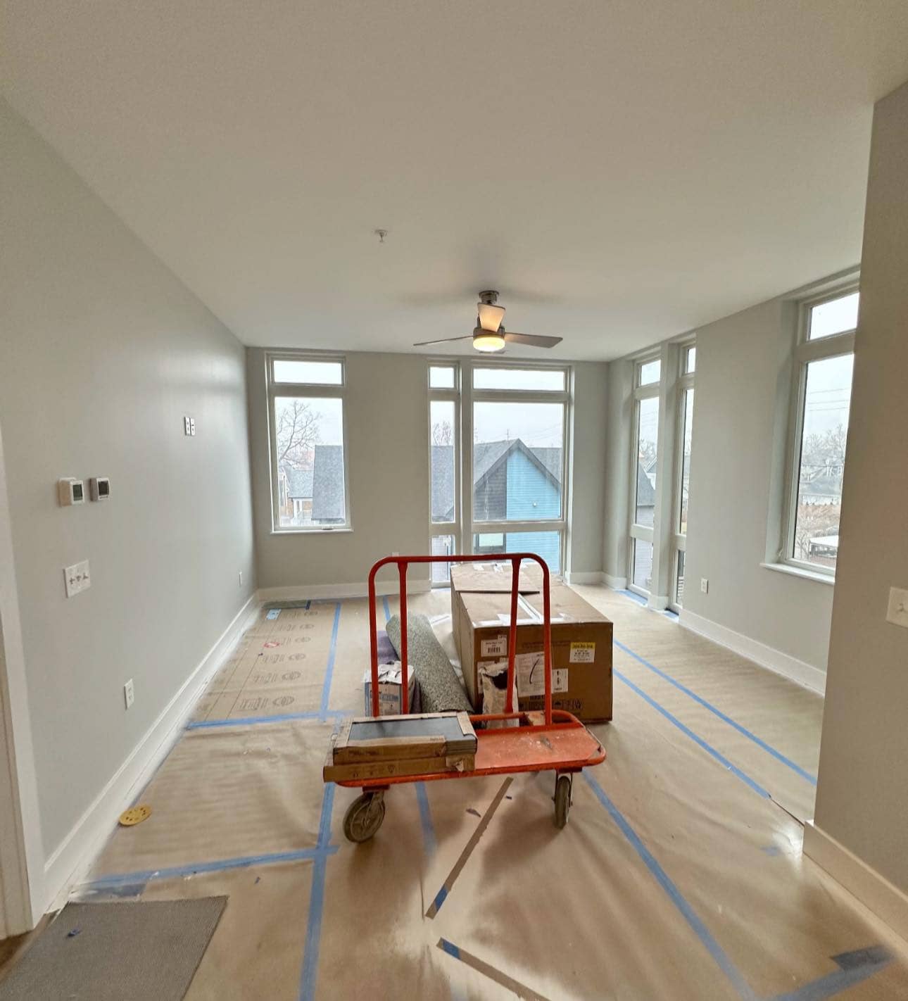 A modern guest bedroom featuring a ceiling fan, soft gray walls, and plush carpeting.