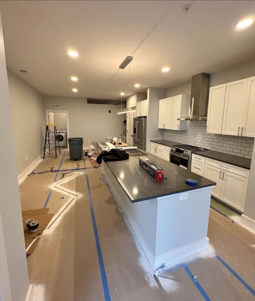 Modern kitchen with white cabinetry, black countertops, a large island, and stainless steel appliances.