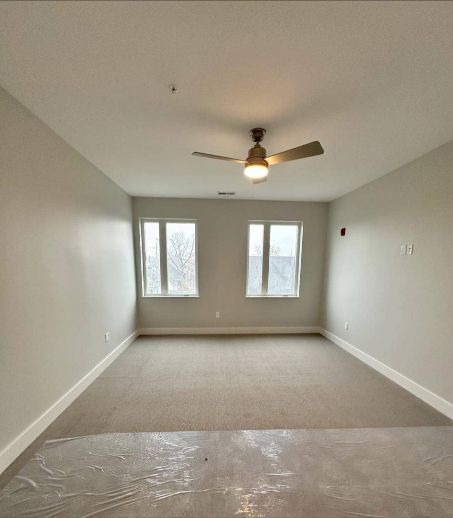 Bright living room featuring large windows, neutral-colored walls, and a ceiling fan.