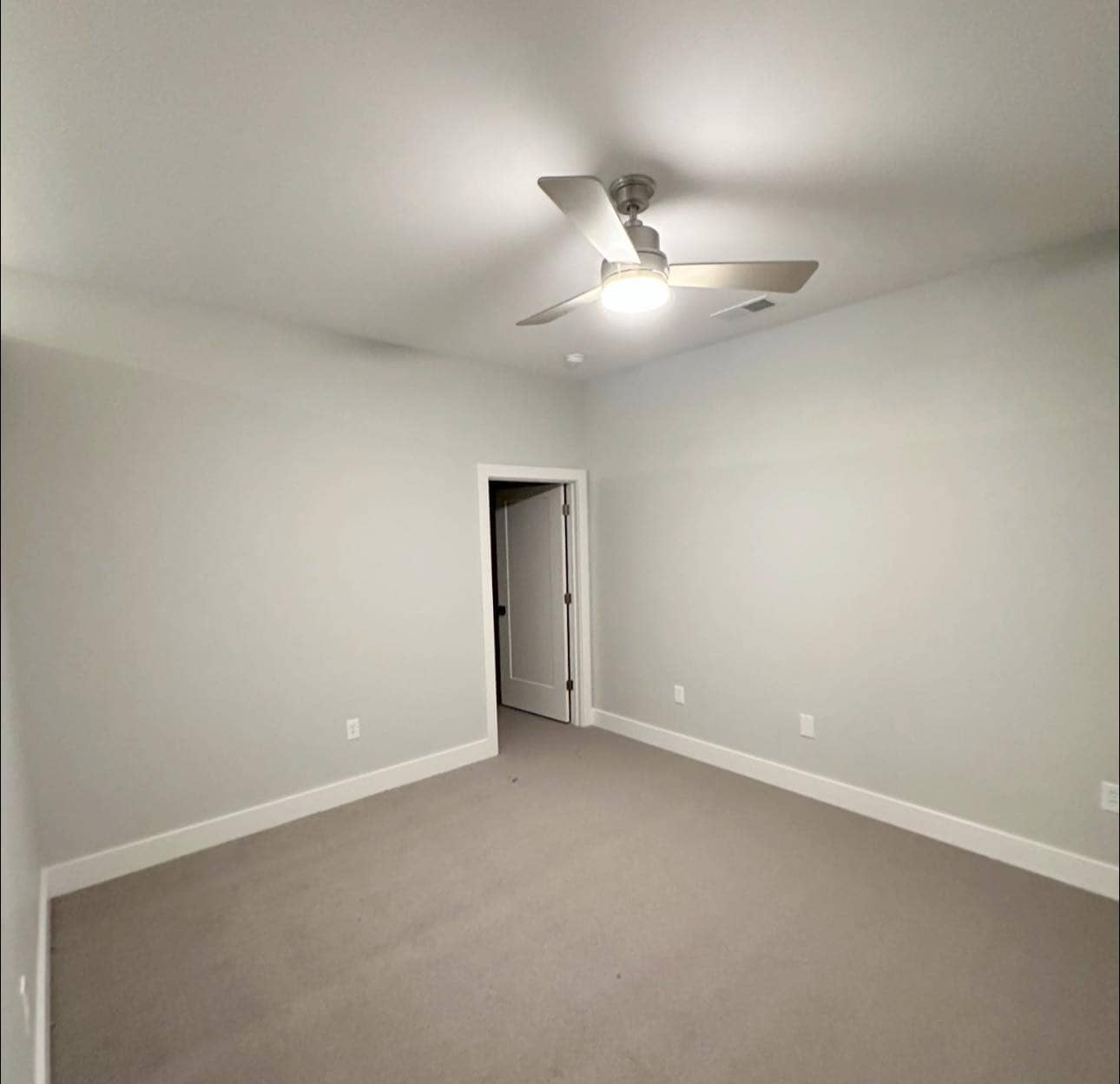 A spacious master bedroom with neutral-colored walls, plush carpeting, and a ceiling fan.